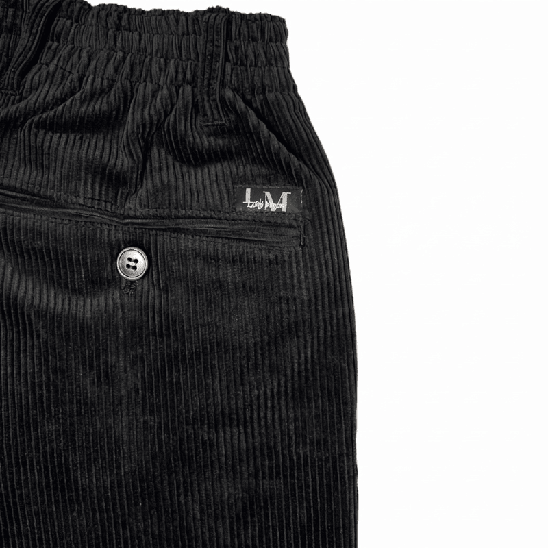Primo piano del tessuto di velluto a coste nero, una tasca posteriore con bottone e l'elastico in vita dei pantaloni