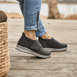 Donna che indossa pantofole New Feet grigio antracite su un pavimento in legno, vista laterale dei piedi