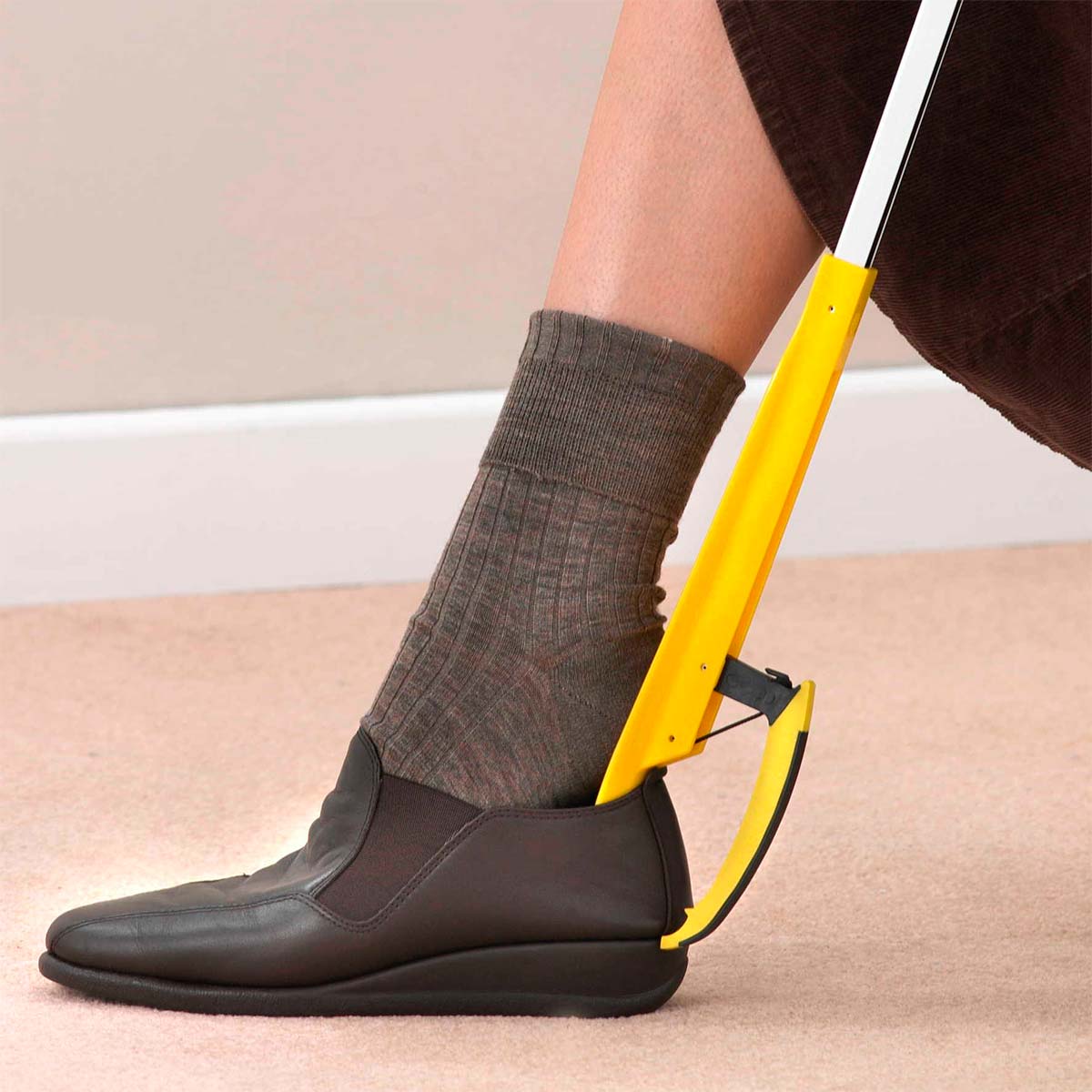 Una persona usa la pinza prendi oggetti gialla come calzascarpe per indossare una scarpa marrone scuro